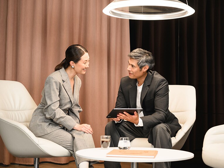 One person showing another person something on a mobile device whilst seated.