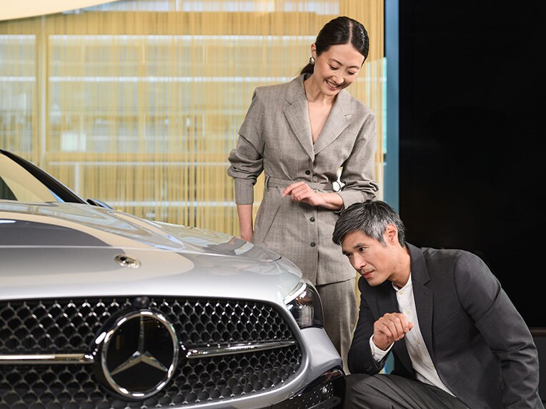 Two people looking closely at the headlight of a Mercedes-Benz vehicle.