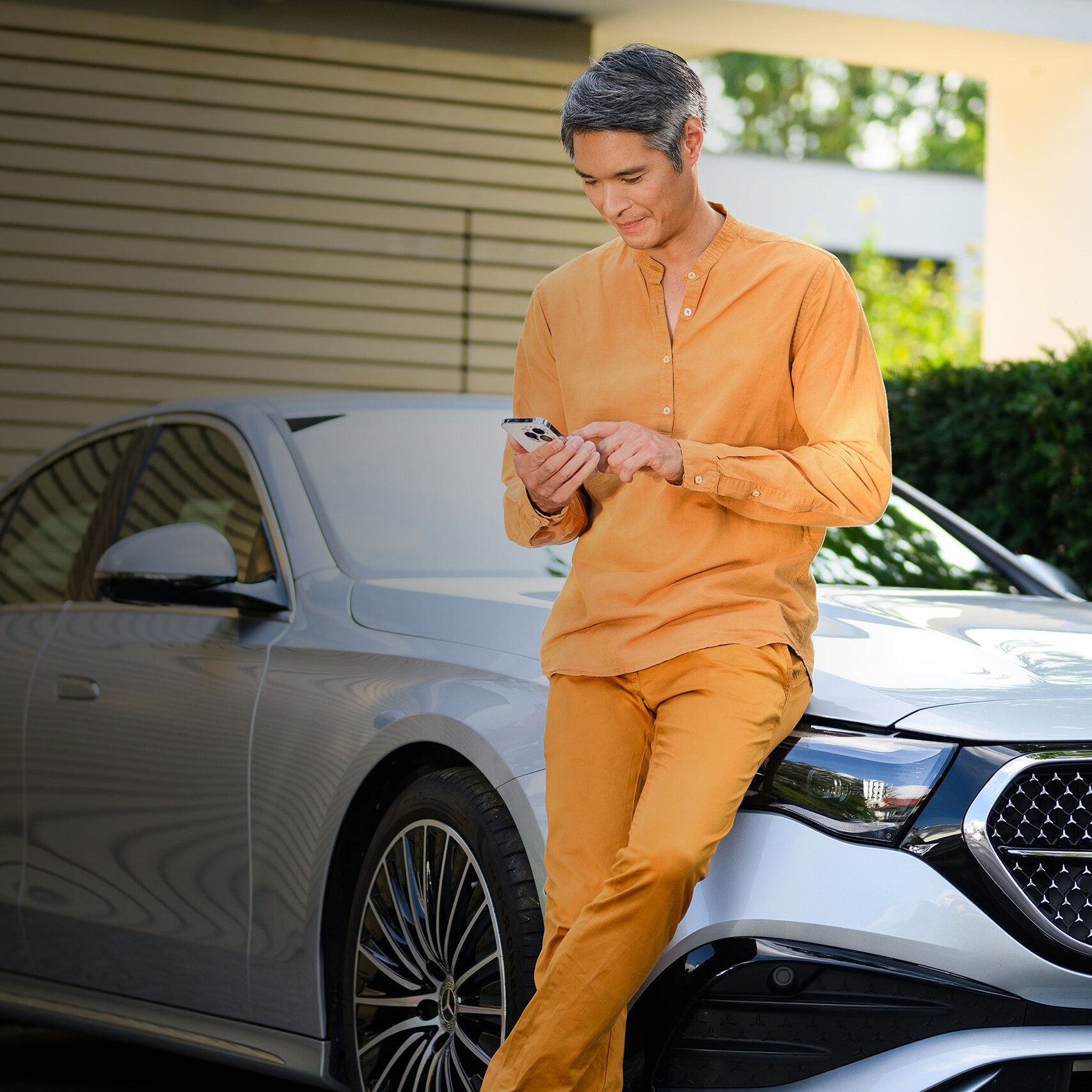 A person leaning against a Mercedes-Benz vehicle, using a mobile device.