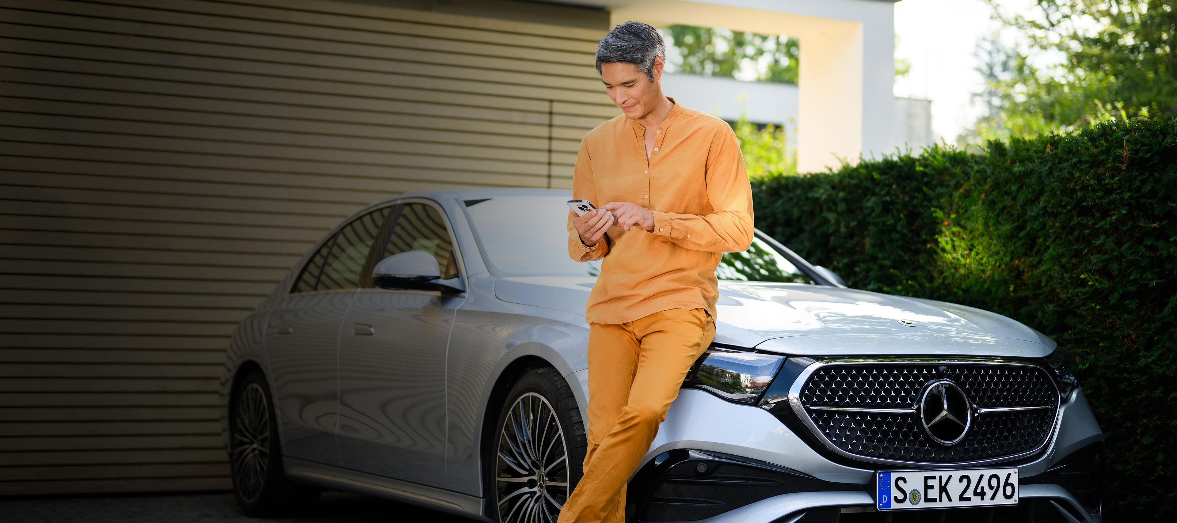 Insurance for your Mercedes-Benz A person leaning against a Mercedes-Benz vehicle, using a mobile device.