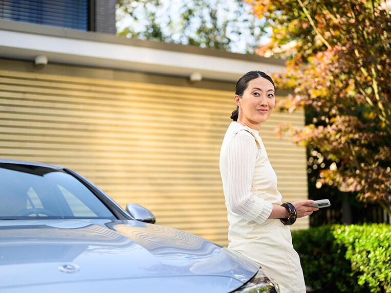 A person leaning against a Mercedes-Benz vehicle, looking at the camera and holding a mobile device.