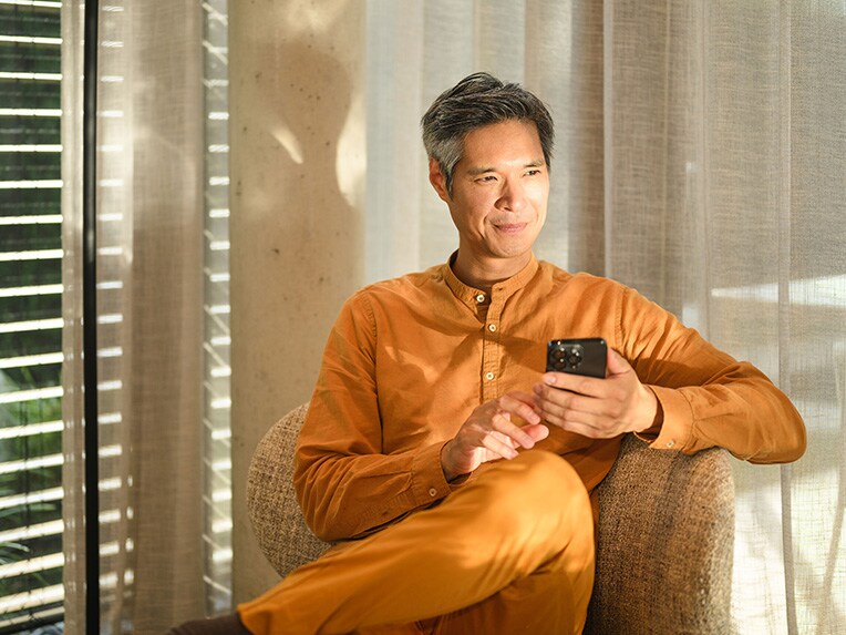 A person sitting in a chair holding a mobile device.