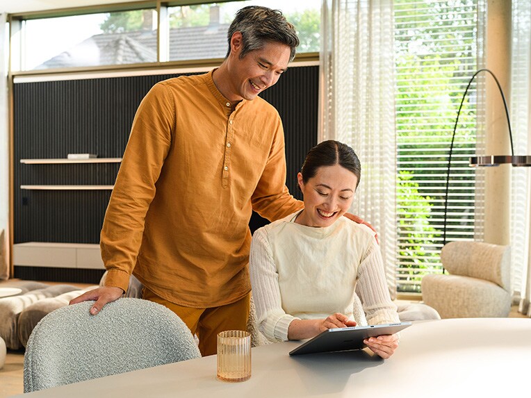  A person sitting at a table looking at their mobile device with someone looking over their shoulder.