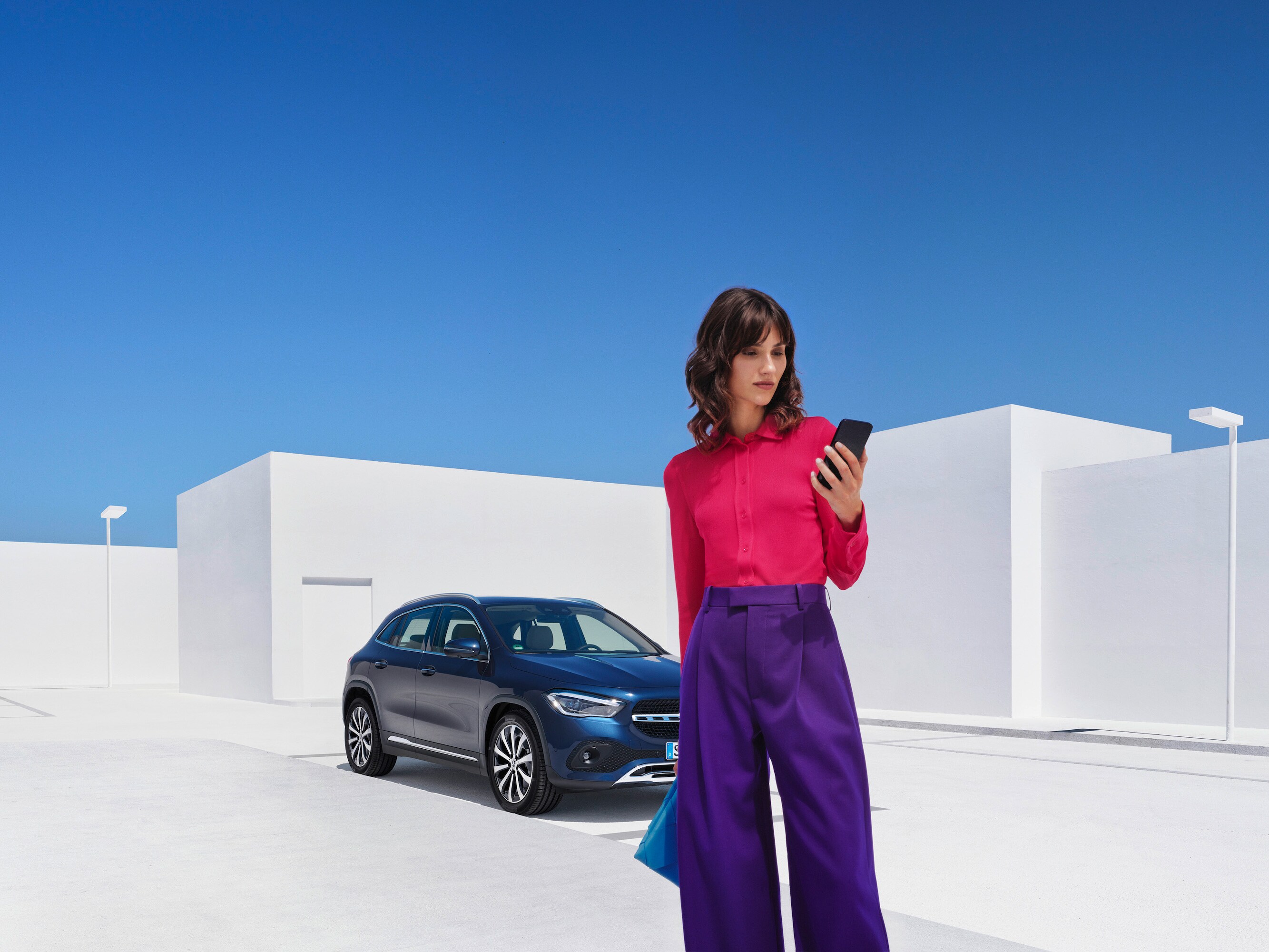 A woman standing in front of her Mercedes-Benz with her smartphone.