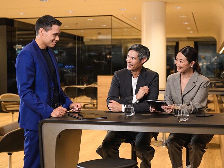 Two people sitting at a table looking at a person standing at the end of the table.