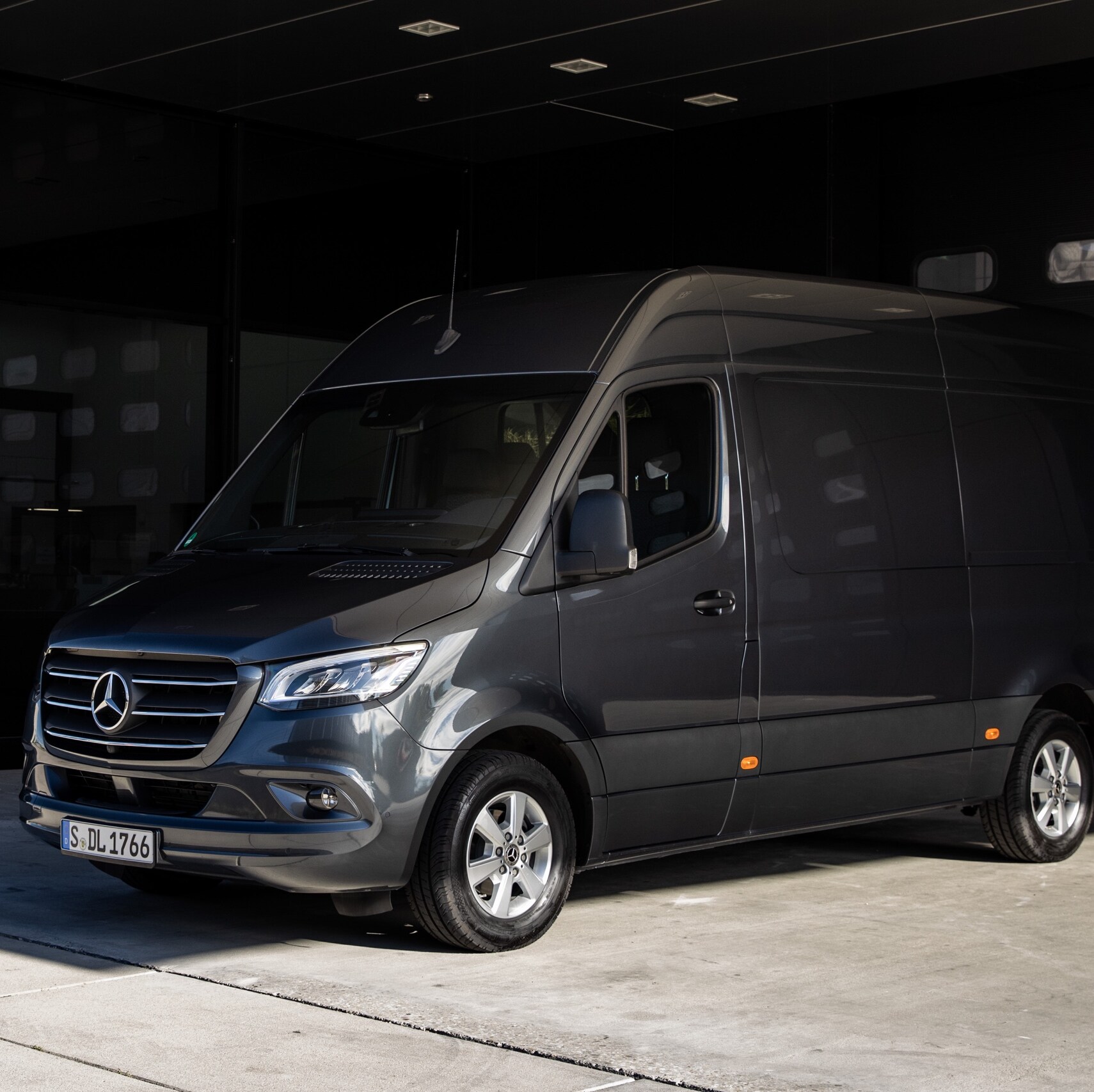 A Sprinter Panel Van from Mercedes-Benz standing in front of a roll-up gate in a modern courtyard.
