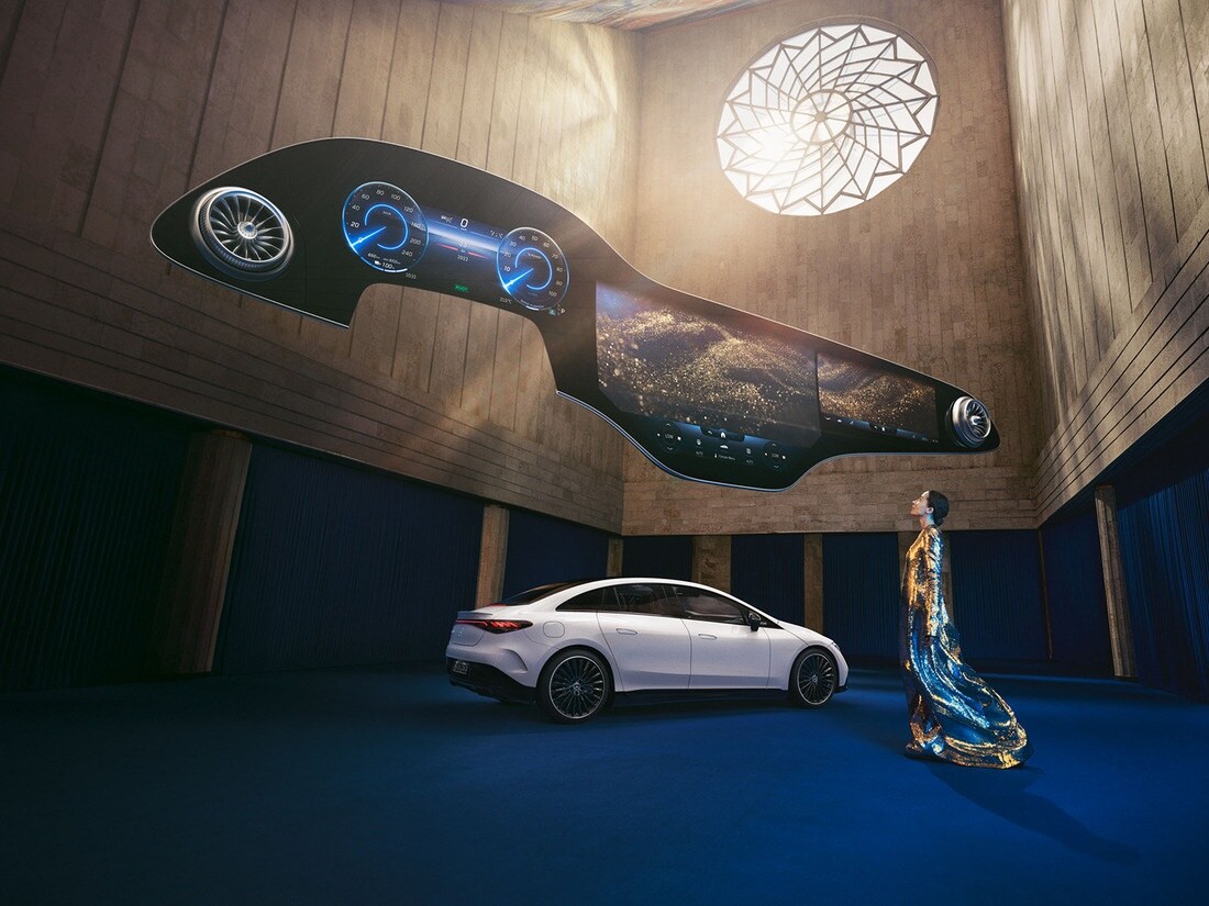 Woman standing in front of Mercedes-Benz EQ vehicle with the Hyperscreen hovering above her.